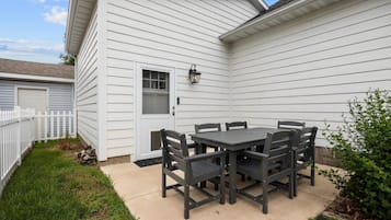 Une terrasse avec une table et des chaises, une clôture blanche et une maison recouverte de bardage.