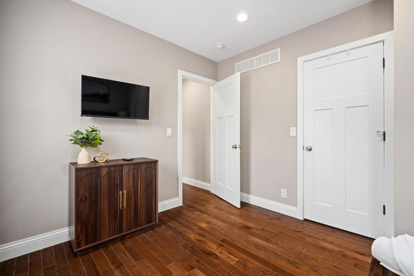 Un pasillo con suelo de madera, puertas blancas y un televisor montado en la pared.