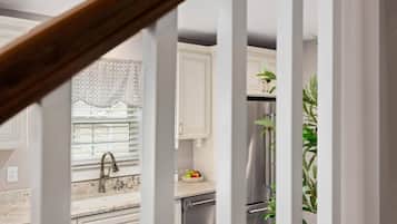 Eine Küche mit weißen Schränken, einem Edelstahlkühlschrank und einem Fenster mit Jalousien.