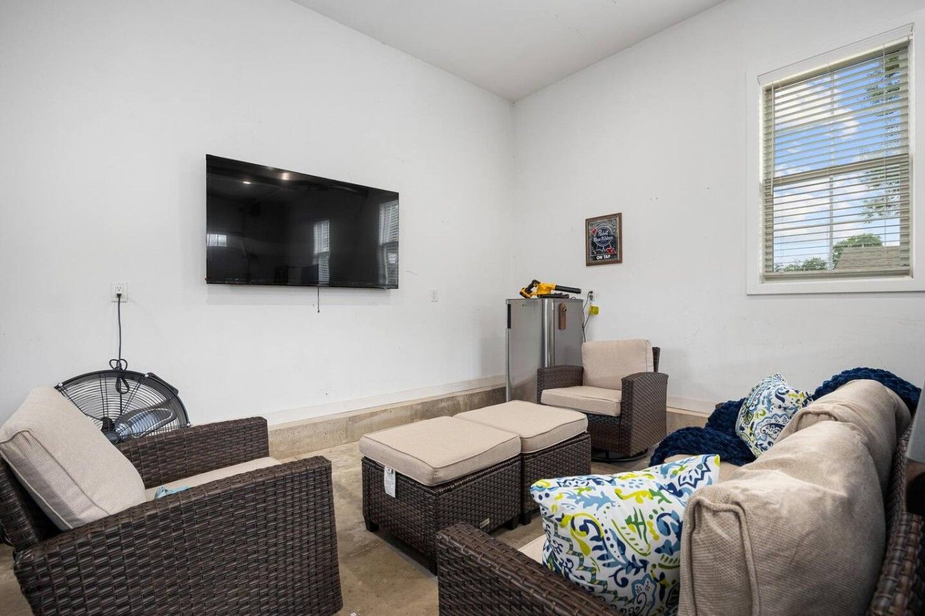 Una sala de estar con muebles de mimbre, un televisor de pantalla plana y una ventana con persianas.