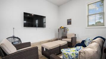 Una sala de estar con muebles de mimbre, un televisor de pantalla plana y una ventana con persianas.