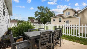 Eine Terrasse mit Tisch und Stühlen, ein weißer Zäun und Häuser im Hintergrund.