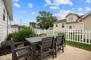 A patio with a table and chairs, a white picket fence, and houses in the background. - Peoria Heights Cottage: Arcade Fun on Columbus (Peoria Heights)