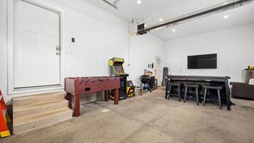Quarto com mesa de pebolim, console de jogos, churrasqueira e televisão fixada na parede.