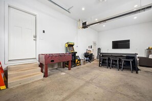 Quarto com mesa de pebolim, console de jogos, churrasqueira e televisão fixada na parede.