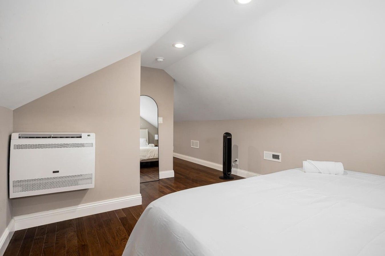 Una habitación de hotel con una cama, un equipo de aire acondicionado, un espejo y un objeto negro en el suelo.