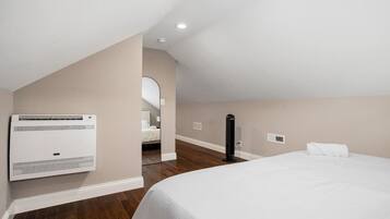 Una habitación de hotel con una cama, un equipo de aire acondicionado, un espejo y un objeto negro en el suelo.