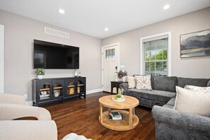 Een moderne woonkamer met een flatscreen televisie, donkere houten vloeren, een grijze bank en een ronde salontafel.