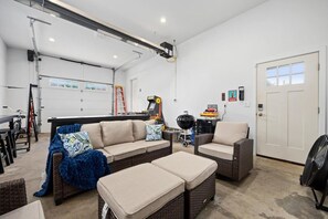 A spacious living area with a sofa, ottoman, and chairs, a grill, and a dining table.