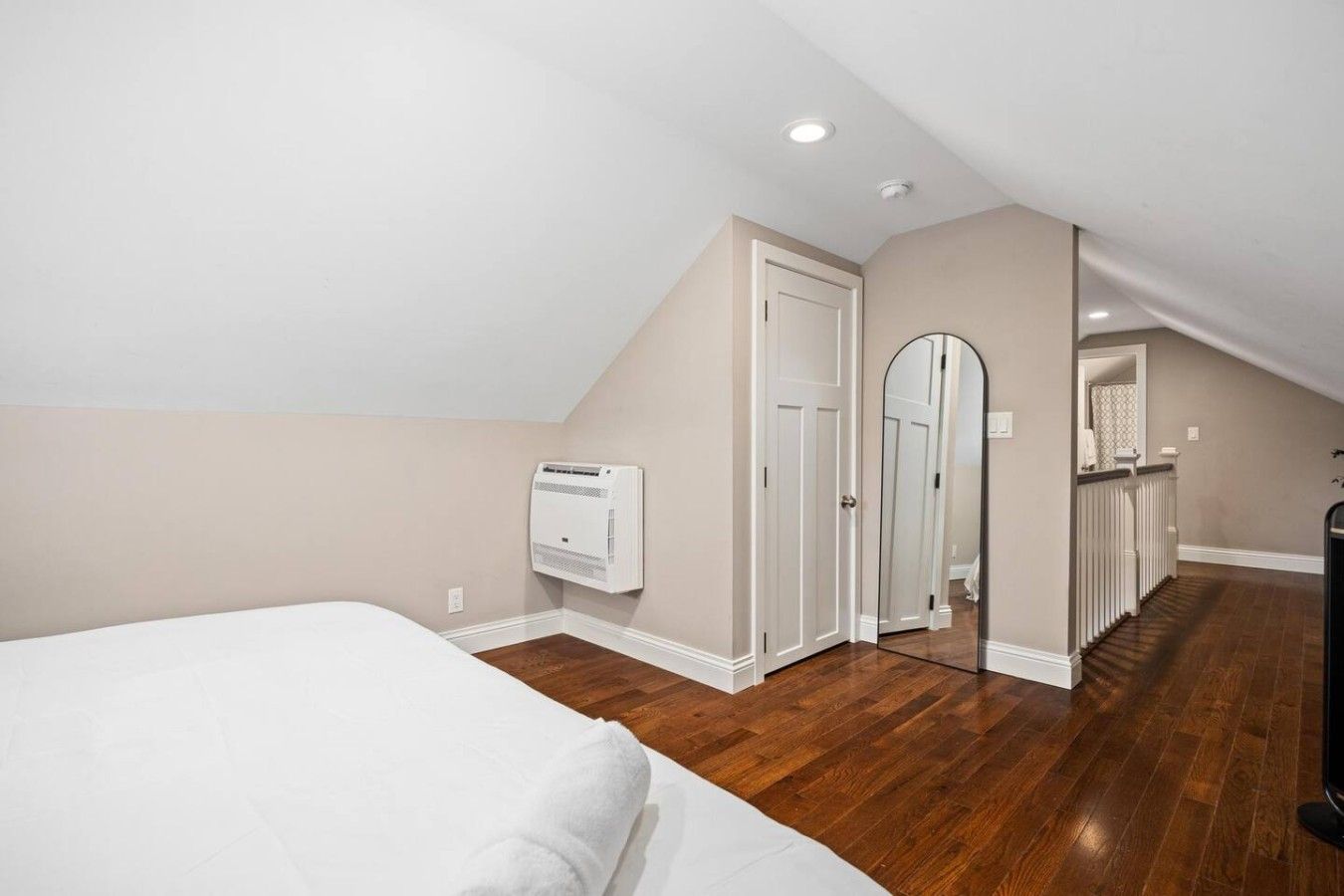 Une chambre à coucher comprenant un lit, un appareil de climatisation, une porte et un couloir menant à une salle de bain.