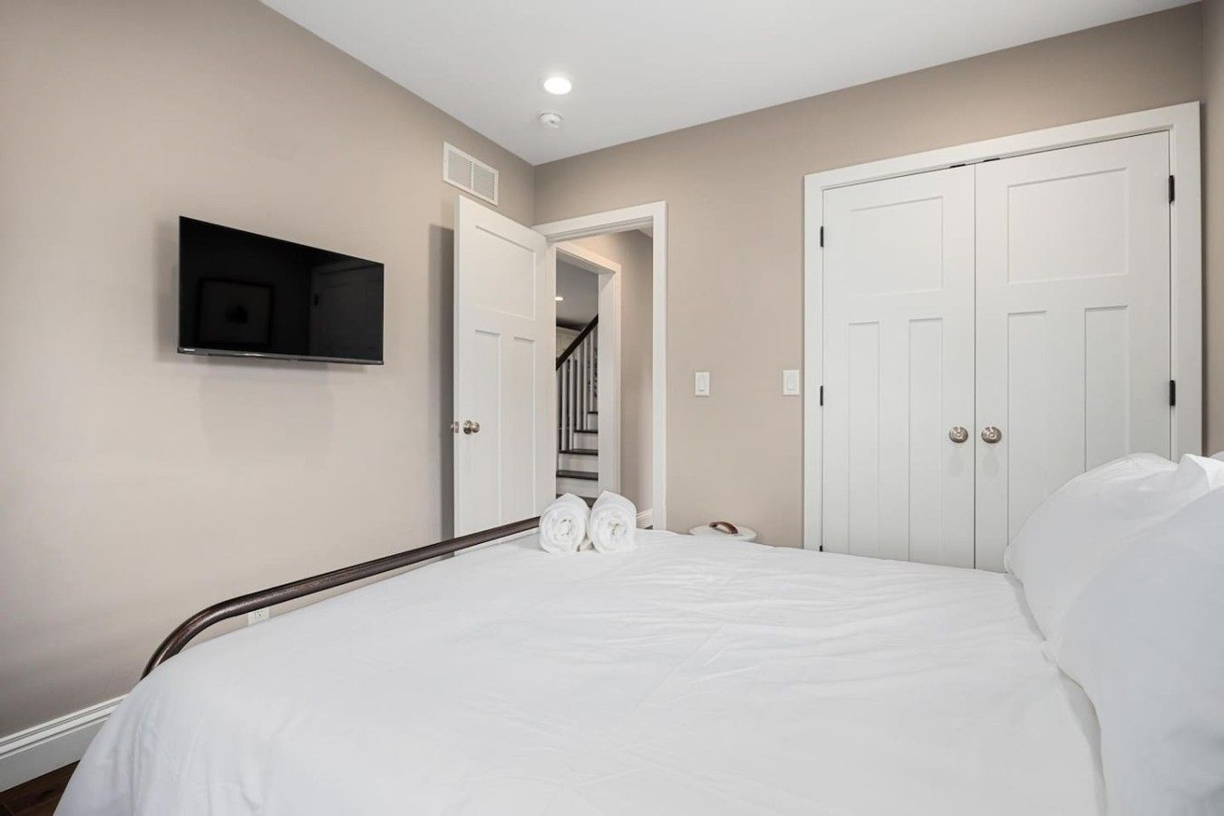 Quarto com cama, televisão fixada na parede e um conjunto de portas brancas.