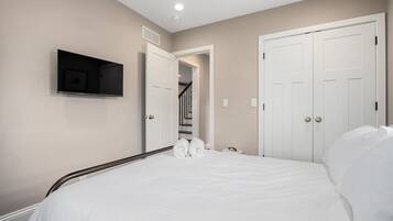 Quarto com cama, televisão fixada na parede e um conjunto de portas brancas.