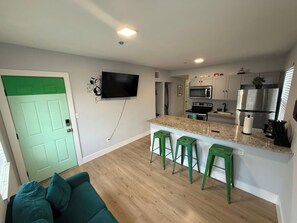 Eine moderne Küche mit Fernseher, Barhocker und einer grünen Tür.