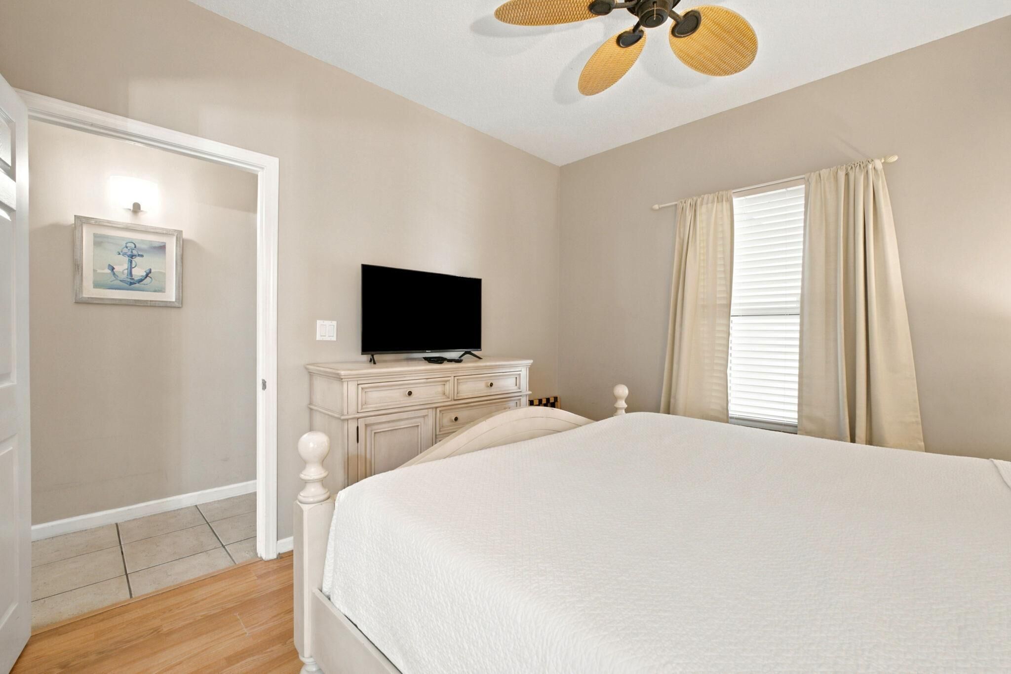 A bedroom with a bed, a television on a dresser, a ceiling fan, and a window with curtains.