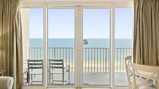 Een kamer met uitzicht op de oceaan, een glazen schuifdeur en twee witte stoelen.