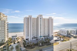 A high-rise hotel with multiple balconies, a parking area, and a beach view. - Windemere 1004 (Pensacola)