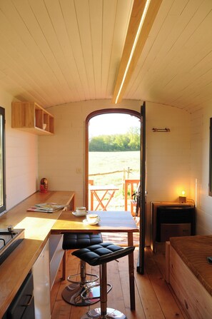 A compact kitchen with a wooden table, bar stool, and a view of a wooden deck outside.
