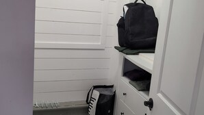 A small storage closet with white doors, a wooden floor, and a black bag on the top shelf.