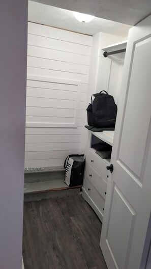 Un petit placard de rangement avec des portes blanches, un plancher en bois et un sac noir posé sur l’étagère supérieure.