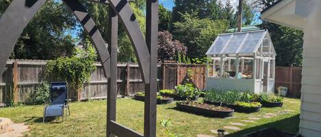 Un jardin avec une serre, une clôture en bois et un banc.