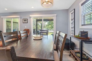 A dining area with a long wooden table, chairs, a chandelier, and a view through glass doors to an outdoor patio. - Lighthouse Lodge Resort - The Red House - Amazing Patio & Lake Views - Outdoor Pool! (Kimberling City)