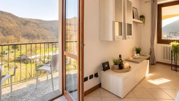 A balcony with a view of a mountainous landscape, a white console table with a vase and candles, and a sliding glass door.