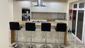 A modern kitchen with a central island, bar stools, stainless steel appliances, and a fire extinguisher. - Impeccable 1-bed House in London (London)