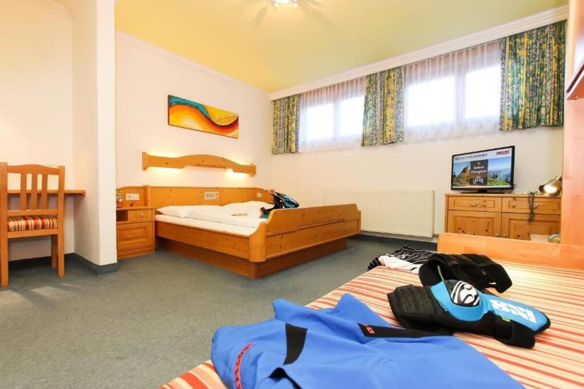 Un dormitorio con una cama de madera, un escritorio, una silla, un televisor y una ventana con cortinas.