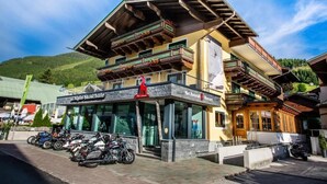 A multi-story building with balconies, a sign for 'Alpin-Schule,' and parked motorcycles. - Hotel Heli's (Hinterglemm)