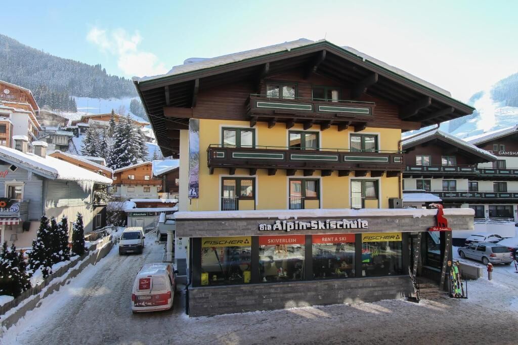 Een meerhoog gebouw met een winkel voor ski verhuur op de begane grond, omgeven door besneeuwde gebouwen en een bergachtige achtergrond.