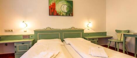 A hotel room with two beds, a green headboard, bedside tables, a desk, and a chair.