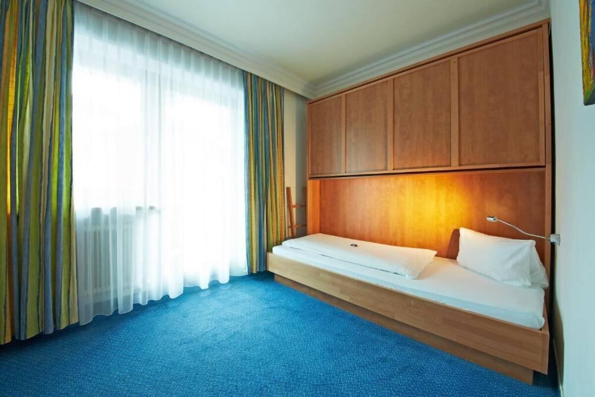 Una habitación con cama, cortinas, cabecera de madera y piso alfombrado.