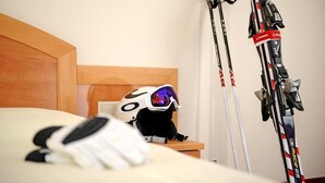 A bed with a wooden headboard, a ski helmet on the bed, and two pairs of skis leaning against the wall. - Hotel Heli's (Hinterglemm)