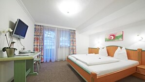 A hotel room with a bed, a desk, a television, and a window with curtains. - Hotel Heli's (Hinterglemm)