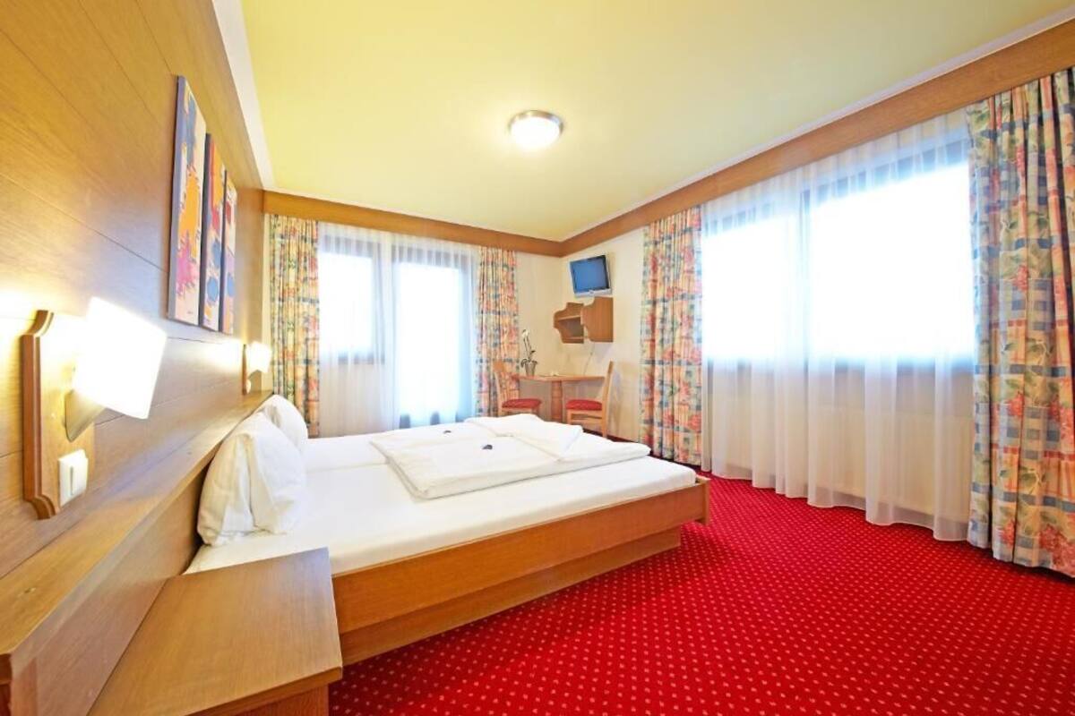 Una habitación de hotel con cama, escritorio, silla, televisor y ventana con cortinas.