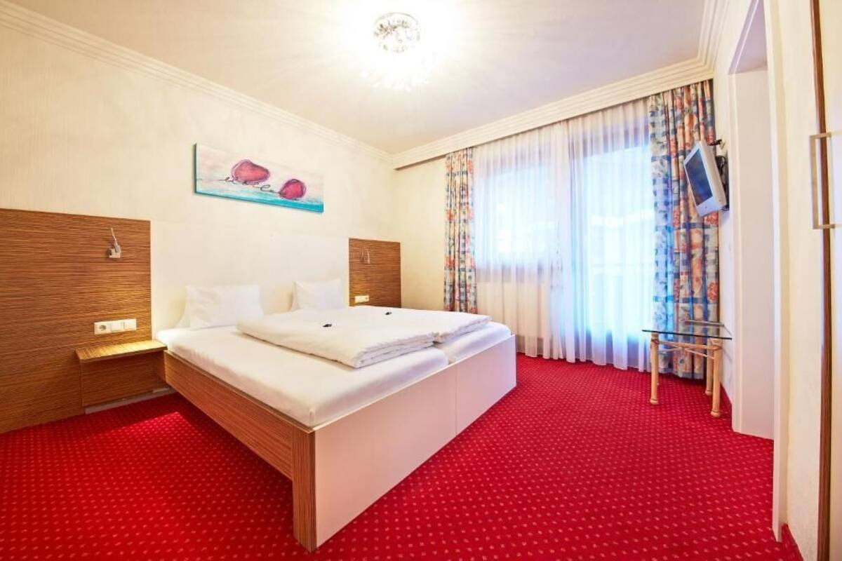 Habitación de hotel con una cama grande, cabecera de madera, un cuadro en la pared y alfombra roja.