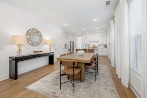 A modern kitchen with white cabinets, a central island, and a dining area with a wooden table and chairs. - Moxie - 1.5 Miles From DT & UofA (Fayetteville)