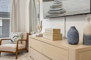 Ein Zimmer mit einem Holzhocker, einem Flachbildfernseher, einem Stapel Kisten und zwei Vasen auf einer Holzkommode.