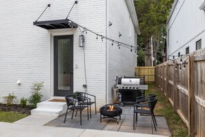 Eine Terrasse mit Grill, Feuerstelle und Gartenmöbeln.