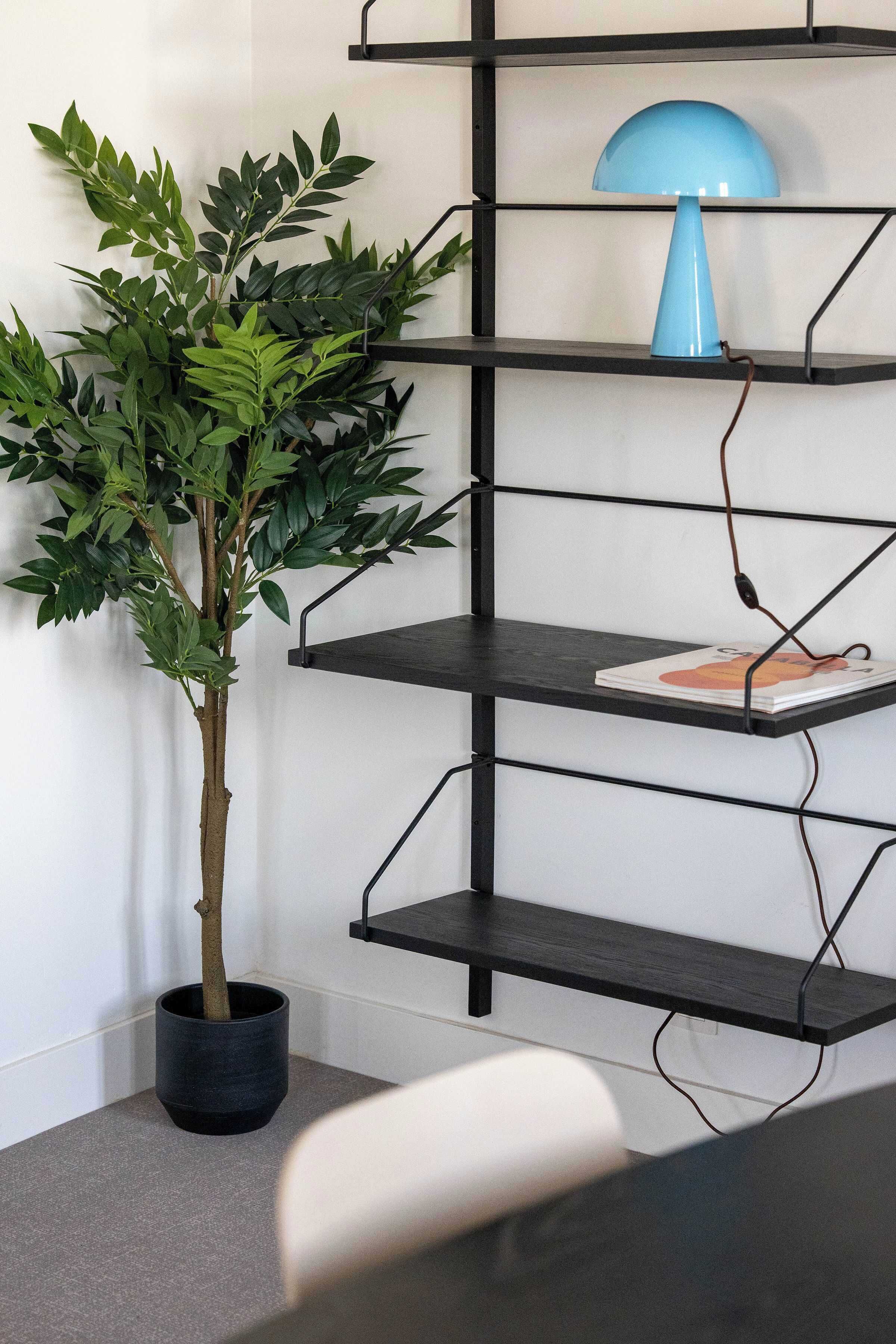 A black metal shelving unit with a blue lamp on the top shelf, a potted plant, and a magazine on the middle shelf.