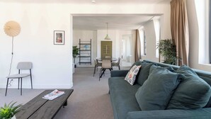 Un salon moderne avec un canapé vert, une table basse en bois, un coin repas avec une table et des chaises, et une plante.