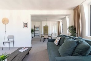 Ein modernes Wohnzimmer mit einem grünen Sofa, einem Holztisch, einem Essbereich mit Tisch und Stühlen sowie einer Pflanze.