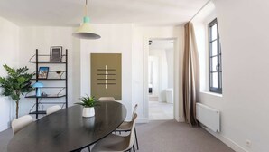 Un espace repas moderne avec une table ronde, des chaises, une suspension, une plante et une bibliothèque.