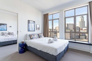 A modern bedroom with a large window, a bed with white bedding, and a city view. - Stylish 2BR Apartment for 6 with Sofa Bed (Antwerpen)