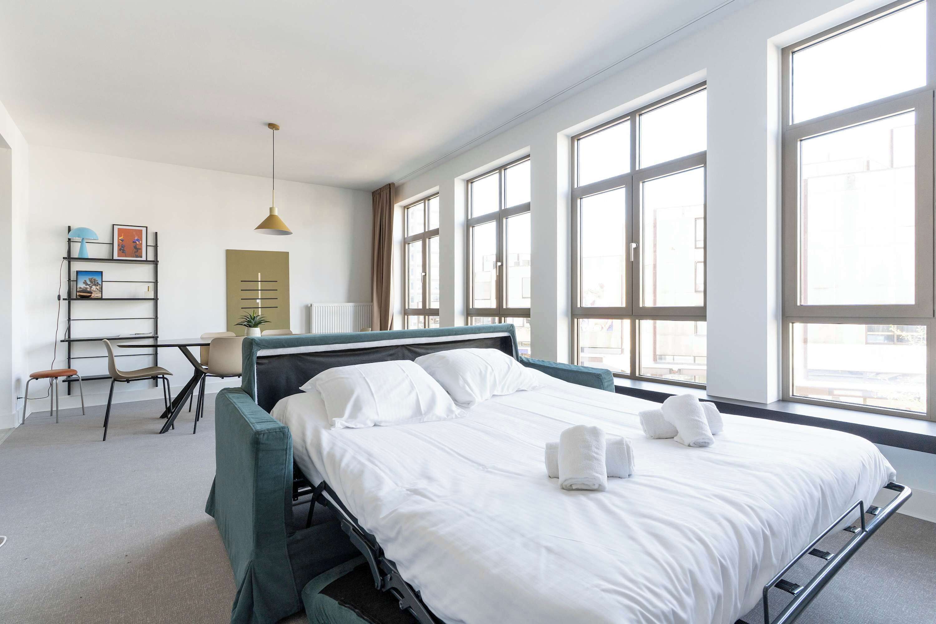 Ein Hotelzimmer mit Bett, Schreibtisch, Stuhl und großen Fenstern.