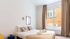 Ein Hotelzimmer mit Bett, Fenster, Heizkörper und einem kleinen Tisch mit Lampe.