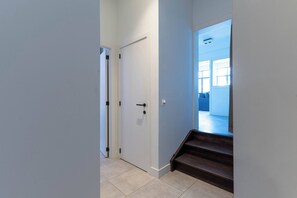 Ein Flur mit einer geschlossenen Tür, einer Treppe und einem Blick in einen Raum mit einem großen Fenster.