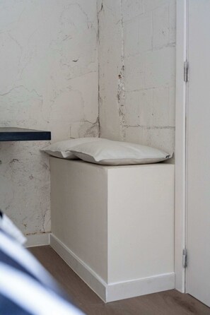 Eine Ecke eines Raumes mit einer weißen Wand, einer weißen Tür und einer weißen Bank mit Kissen.