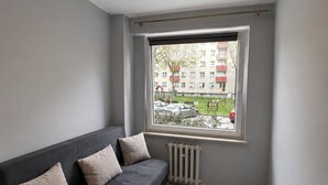 Una sala de estar moderna con un sofá gris, un radiador y una ventana con vista a una zona residencial.