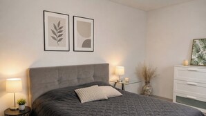 Un dormitorio con una cama grande, mesitas de noche con lámparas, un aparador y cuadros en la pared.